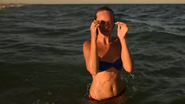 Joven mujer sexy nada en el mar acaricia su cuerpo en bikini traje de baño al atardecer — Vídeos de Stock