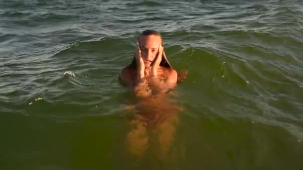 Joven mujer sexy nada en el mar en grandes olas en bikini traje de baño al atardecer — Vídeos de Stock