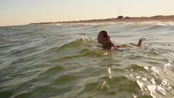 Giovane donna sexy nuota in mare sulle grandi onde in bikini costumi da bagno al tramonto — Video Stock