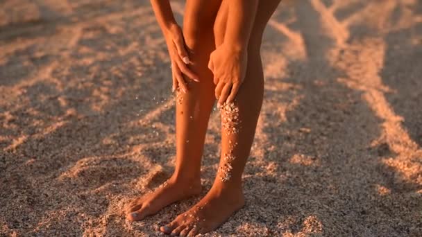 Jeune femme nettoyer les jambes bronzées minces coquillages collants cailloux et sable. au ralenti — Video