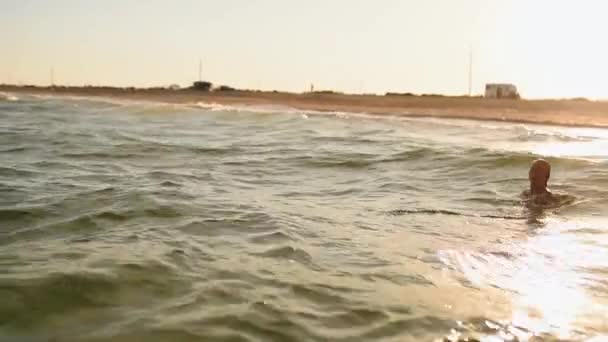 Ung sexig kvinna simmar i havet på stora vågor i bikini badkläder vid solnedgången — Stockvideo