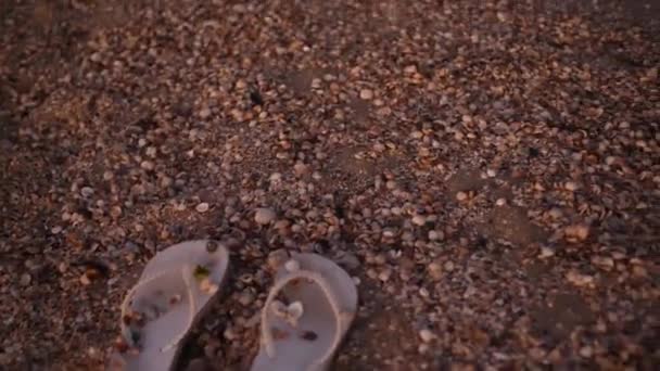 Фліп-флоп в черепашках і пісок на березі штормового моря з хвилями Після заходу сонця — стокове відео