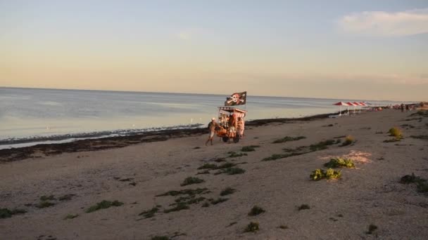 Sprzedawcy ulicznego jedzenia na plaży. Piraci jeżdżą wózkiem na morzu z flagą piratów.. — Wideo stockowe