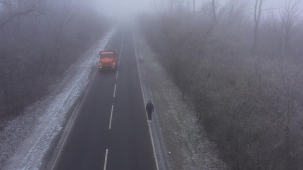 Grande caminhão laranja dirigindo ao longo da estrada. homem corre ao longo da estrada em tempo nebuloso. Vídeo aéreo 4K de drone — Vídeo de Stock