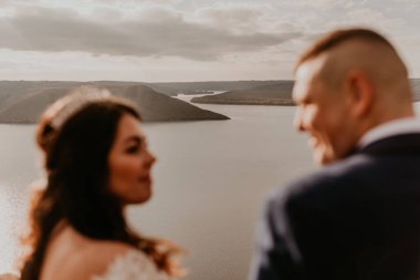 Beyaz elbiseli ve takım elbiseli, sevgi dolu bir çift yazın nehrin üstündeki dağda yürür. gün batımı ve gün doğumu. Kayalıklardaki adam ve kadın adaların arka planında