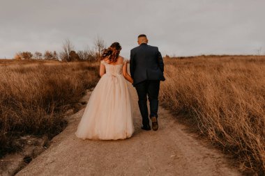 Aşık çift, beyaz elbiseli ve takım elbiseli yeni evliler yazın bir tarlada uzun çimlerde yürüyorlar. Erkek ve kadın el ele tutuşuyor