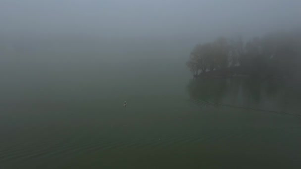 Az ember egyedül lebeg egy táblán egy folyón egy nagyon sűrű ködben. — Stock videók