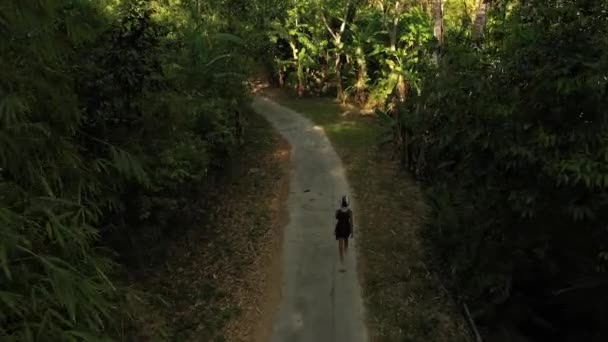 Kobieta w kasku motocyklowym spaceruje wzdłuż drogi w środku zielonej ciemnej dżungli — Wideo stockowe