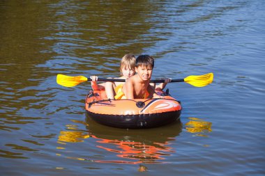 İki erkek şişme lastik teknede eğleniyor 