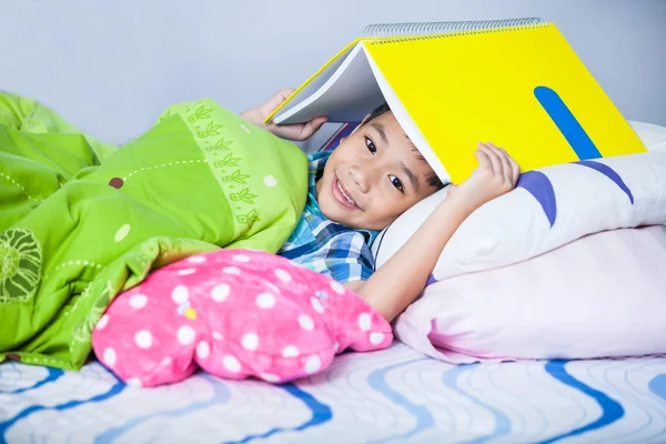 Azjatycki chłopiec obejmujące głowę z książki i uśmiechnięty. Koncepcja kształcenia — Zdjęcie stockowe