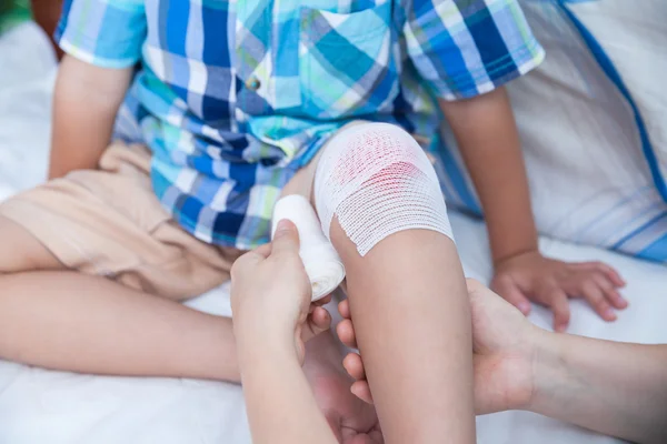 Child injured. Mother bandaging son's knee. — Stock Photo, Image