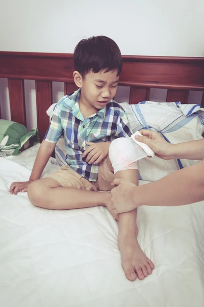 Дитина постраждала. Мати перев'язує коліно сина. Вінтажний стиль . — стокове фото