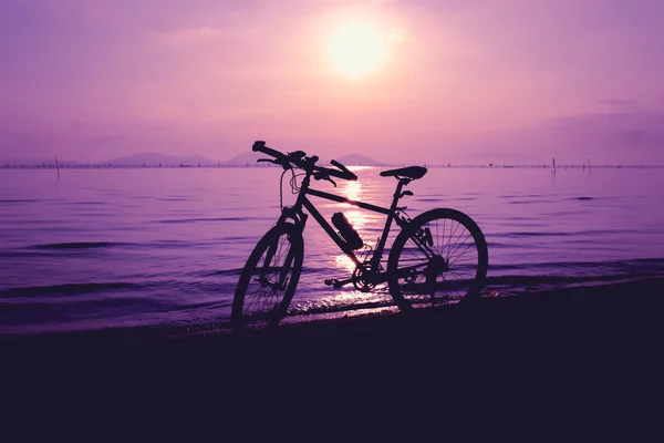 Силует велосипеда на пляжі проти барвистого заходу сонця в морі — стокове фото