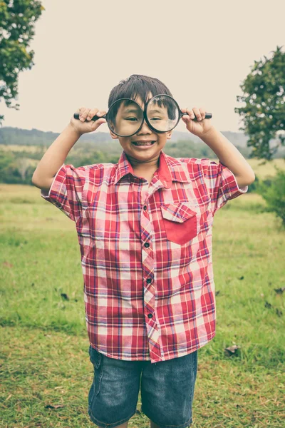 Young boy exploring nature with magnifying glass. Outdoors. Vintage style. — Stock Photo, Image