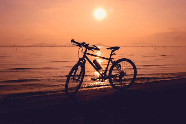 Silhueta de bicicleta na praia contra o pôr do sol colorido no mar . — Fotografia de Stock