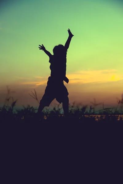 Sylwetka dziecka skoki wobec zachód słońca. Chłopiec, ciesząc się widokiem. — Zdjęcie stockowe