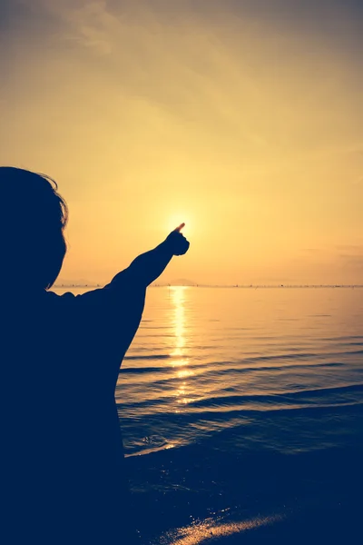 Силуэт задний вид женщины расслабиться на берегу моря и указывая на солнце . — стоковое фото