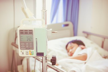 Asyalı çocuk hasta yatağının üzerinde infüzyon pompa intravenöz IV damlalıkla yalan