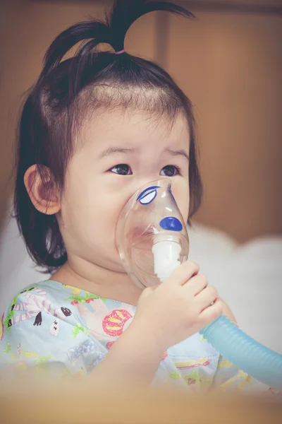 アジアの子供は、喘息の治療のためマスクの蒸気吸入器を保持しています。. — ストック写真