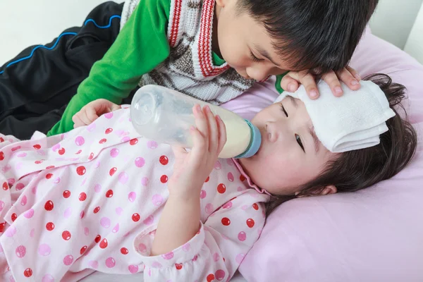 Enferma hermana mintiendo y chupar la leche en la cama, hermano amable mantener la vigilancia sobre un enfermo de cerca . — Foto de Stock