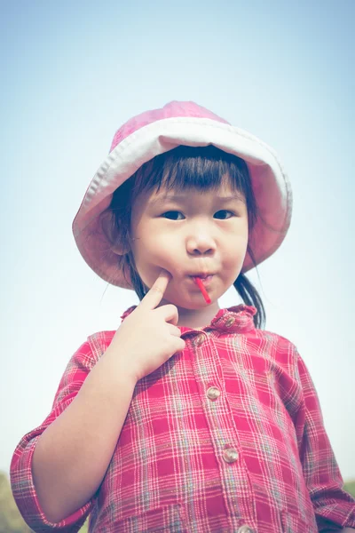 Χαριτωμένο μικρό ασιατικό κορίτσι τρώει ένα γλειφιτζούρι σε φόντο της φύσης το καλοκαίρι. — Φωτογραφία Αρχείου