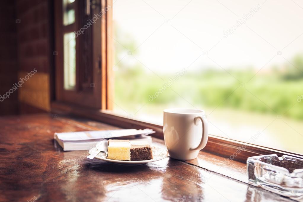 Cake and cup of coffee on wooden table near window sill.