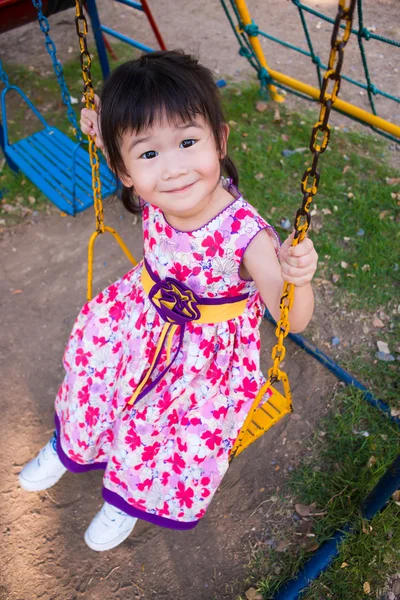 Чарівна дівчина розважається на гойдалках у парку. Сонячне світло у дітей — стокове фото