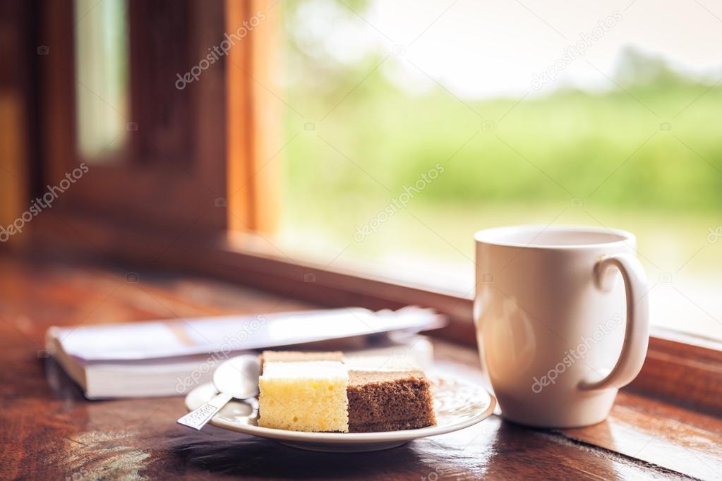 Cake and cup of coffee on wooden table near window sill. Time wi