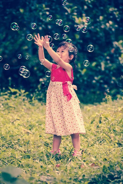 Asian girl catches soap bubbles on nature background. Outdoors. — Stock Photo, Image