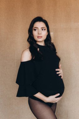 Siyah bir beden ve tayt içinde kumaş arka planı olan bir fotoğraf stüdyosunda hamilelik fotoğrafı çekimi.