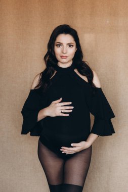 Siyah bir beden ve tayt içinde kumaş arka planı olan bir fotoğraf stüdyosunda hamilelik fotoğrafı çekimi.