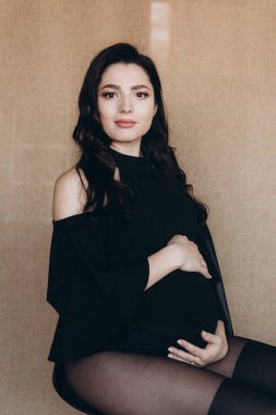 Siyah bir beden ve tayt içinde kumaş arka planı olan bir fotoğraf stüdyosunda hamilelik fotoğrafı çekimi.