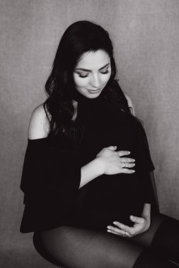 Siyah bir beden ve tayt içinde kumaş arka planı olan bir fotoğraf stüdyosunda hamilelik fotoğrafı çekimi.