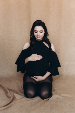 Siyah bir beden ve tayt içinde kumaş arka planı olan bir fotoğraf stüdyosunda hamilelik fotoğrafı çekimi.