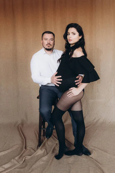 Pregnancy photo session in a photo studio with a fabric background in a black bodysuit and tights