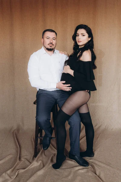 Pregnancy photo session in a photo studio with a fabric background in a black bodysuit and tights