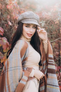 Güzel ve şık bir kız mankeni bej bir elbise ve parkta ekose şeklinde bir eşarp giyiyor.