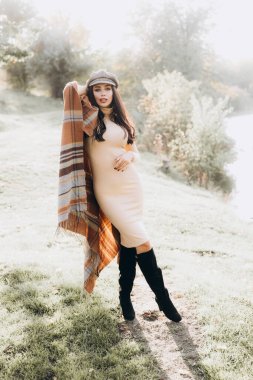 Güzel ve şık bir kız mankeni bej bir elbise ve parkta ekose şeklinde bir eşarp giyiyor.