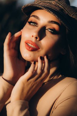 Güzel ve şık bir kız mankeni bej bir elbise ve parkta ekose şeklinde bir eşarp giyiyor.