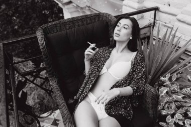 Balkondaki kız beyaz iç çamaşırıyla sigara içiyor.