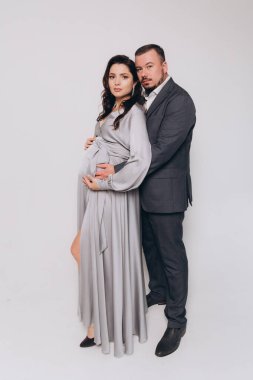 Güzel bir çiftin hamilelik fotoğrafı. Gri elbiseli ve takım elbiseli müstakbel ebeveynler.