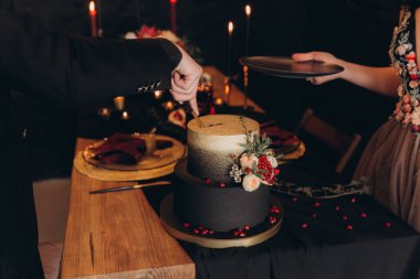 Siyah dekorlu şölen masası, mumlar, pasta ve çiçekler, marsal ve garnet, altın çatal bıçak takımı.