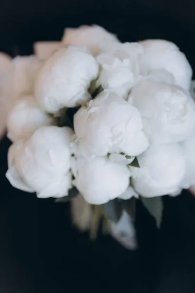 Beautiful white wedding bouquet of peonies on a black chair with a dress and a veil
