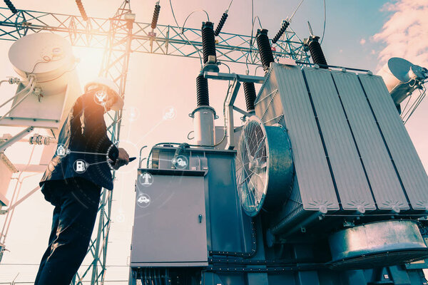 Businessman wearing a black suit, standing looking at a large power transformer with orange sunlight and white sky to be background, Concept about business people who want to invest in energy.