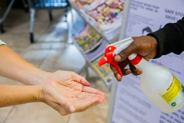 南アフリカのケープタウン 2020年12月10日 ウイルスの拡散を防ぐためにアルコールスプレー消毒器ボトルで店の入り口で顧客の手を消毒するスタッフ — ストック写真
