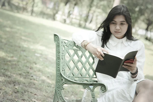 Stok fotoğraf onun kahve kupa yumuşak odak vintage tarzı tutan bir kitap okuma parkta oturan kadın — Stok fotoğraf