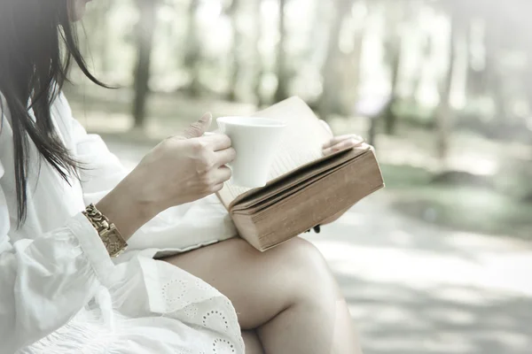 Stock Photo Woman sitting on the park reading a book holding her coffee mug soft focus vintage style — Stock Photo, Image