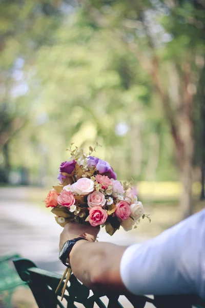 Stock Photo człowiek z bukietem kwiatów i siedzi na ławce w stylu vintage soft focus park — Zdjęcie stockowe