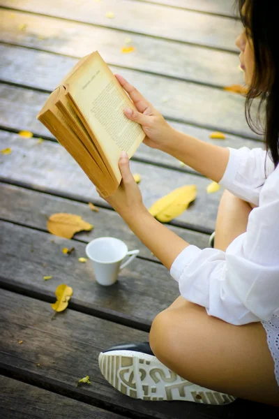 Sevimli genç kadın parkta üzerinde oturan ve kitap yumuşak f okuma — Stok fotoğraf