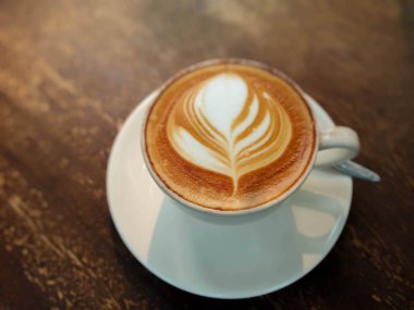 Beyaz bardakta kahve, ahşap masada, arka planda ışıklandırma. Sıcak bir ton.